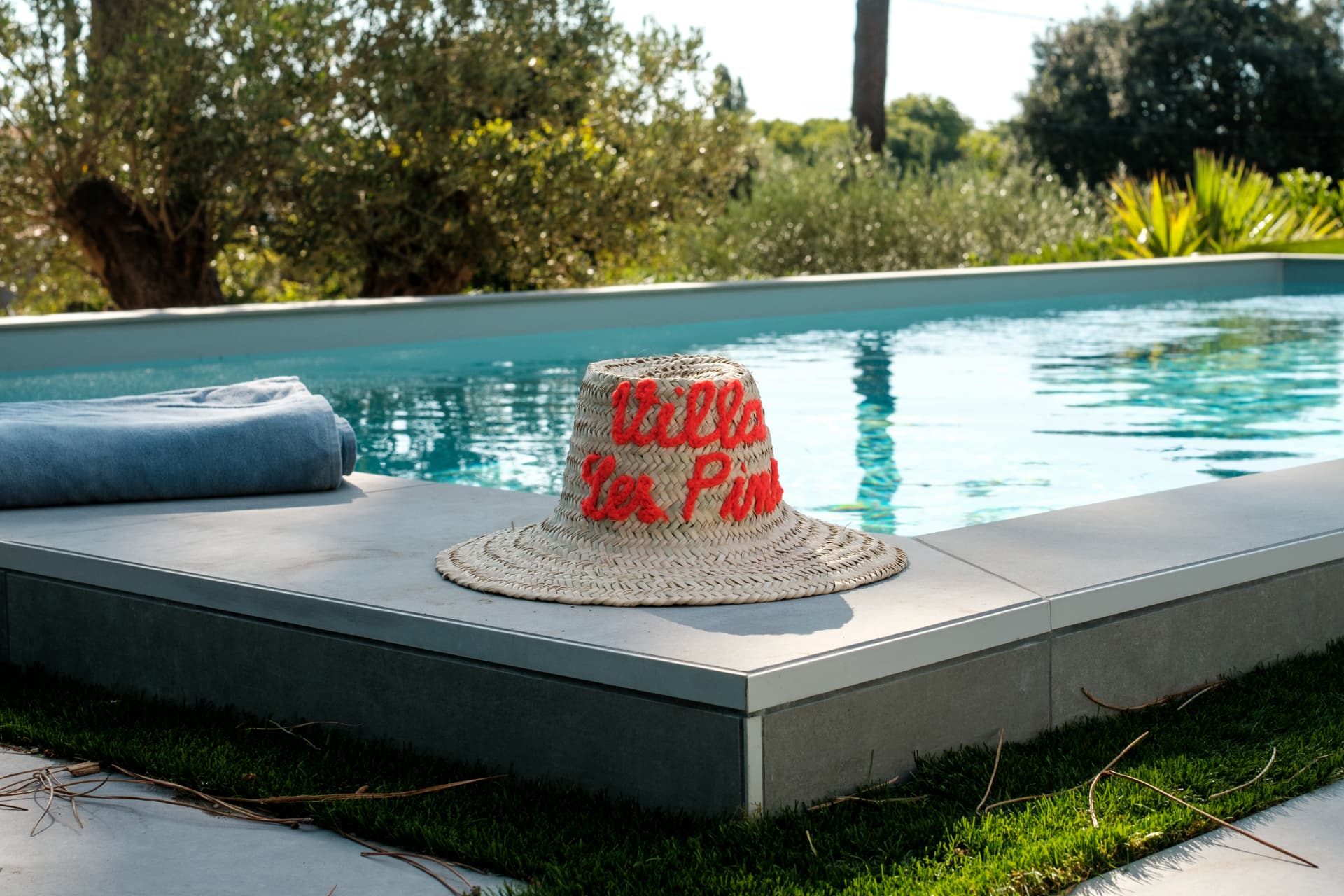 Chapeau de paille sur le bord d'une piscine turquoise, oliviers et verdure en arrière-plan